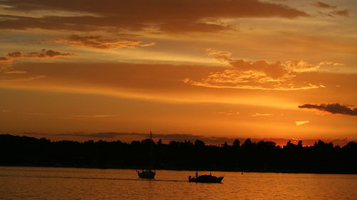 Silhouette boat sailing on river against dramatic sky during sunset