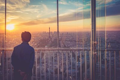 Rear view of man standing by cityscape against sky during sunset