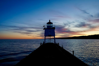 Silhouette lighthouse by sea against sky during sunset