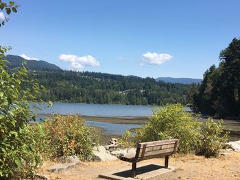 Bench by lake against sky