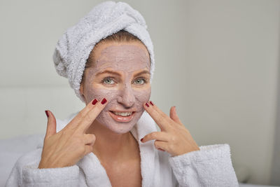 Close-up portrait of smiling woman applying facial mask