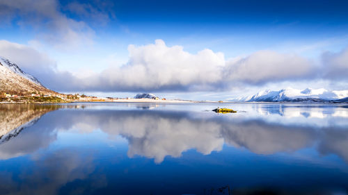 Blue sky, clouds and white snowy mountains, reflecting in the water