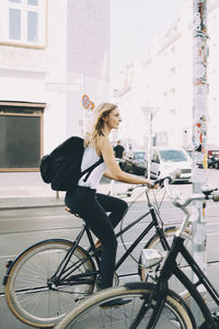 Side view of young woman riding bicycle on street in city