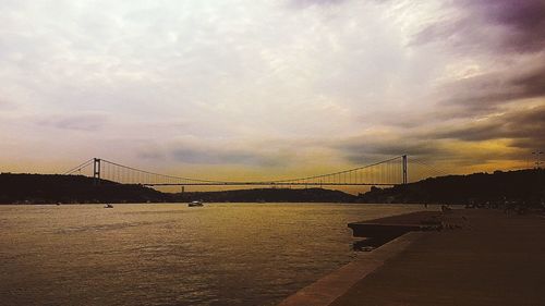 Suspension bridge over river against cloudy sky