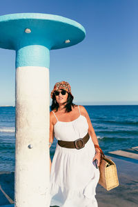 Attractive woman with colorful hat, wicker bag and sunglasses looking at the camera in a summer day.