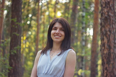 Portrait of smiling young woman standing against trees in forest