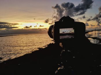 Close-up of silhouette camera on beach against sky during sunset