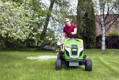 Young man riding lawn mower at grassy field