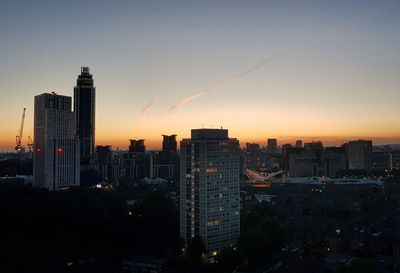 Illuminated buildings in city against sky during sunset