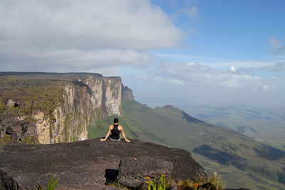 Rear view of man sitting on rock against sky