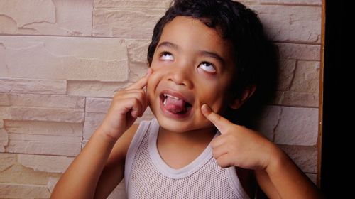 Close-up of funny boy making face against wall