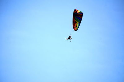 Low angle view of people paragliding against clear blue sky