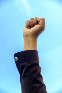 Cropped image of person with hand raised against blue sky