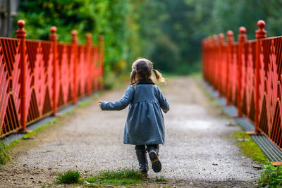 Little girl is running in the forest on a red bridge wearing coat and boots