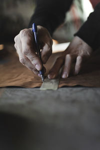 Crop hands of tailor with pen and line measuring textile on workplace