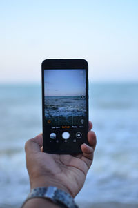 Close-up of hand holding smart phone against sea