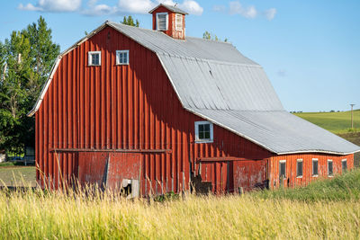 Barn on field by building against sky