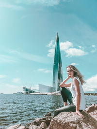 Woman sitting by sea against sky