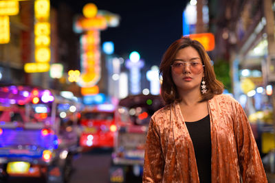 Portrait of woman standing against illuminated city at night