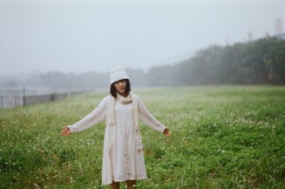 Young woman with arms outstretched standing on grassy field