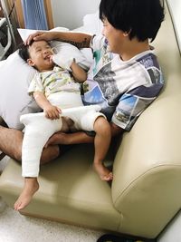 High angle view of father carrying injured boy while sitting on sofa at hospital