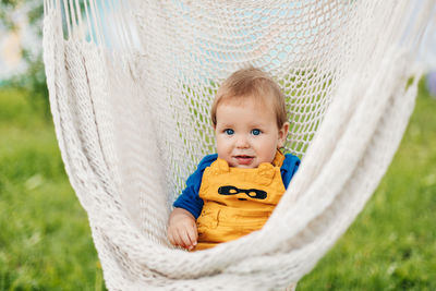 A little boy sits in a hammock and looks at the camera on a summer day in the garden