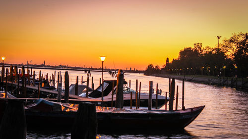 Boats moored in canal against sky during sunset