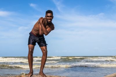 Full length of shirtless man standing in sea against sky