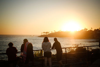 People looking at sea against sky during sunset