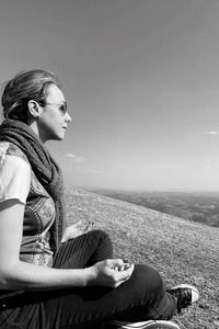 Side view of woman sitting on land against sky