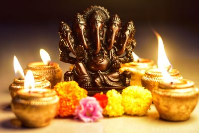 Close-up of ganesha idol with flowers and candles on table