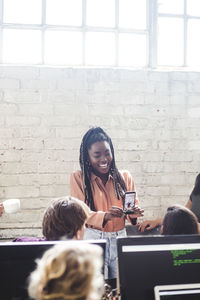 Cheerful young businesswoman showing mobile phone to computer experts at it firm