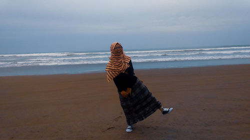 Cheerful girl standing on beach against sky