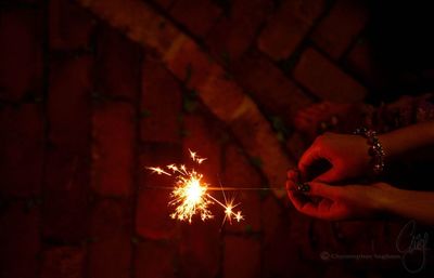 Cropped hands of woman holding illuminated sparklers at night