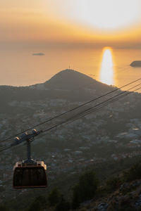 Overhead cable car over sea against sky during sunset