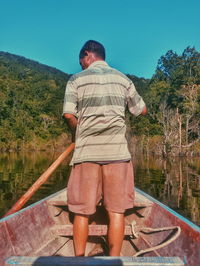 Rear view of man standing by lake against sky