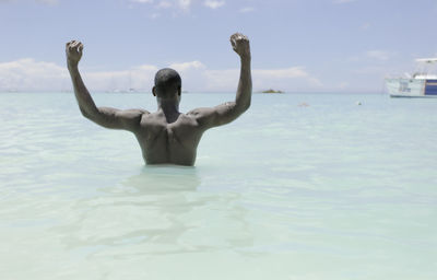 Muscular african american tourist in tank top raising arms while standing inside clean sea water