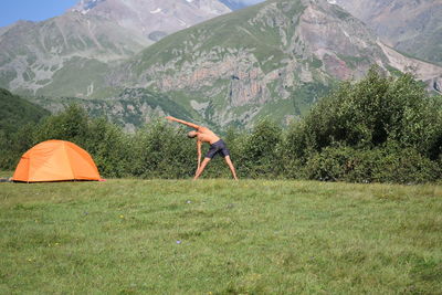 Rear view of man doing yoga in field against mountain