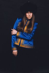 Portrait of young woman wearing costume standing against black background