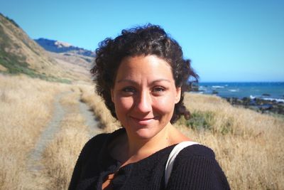 Close-up portrait of young woman standing on field against clear blue sky