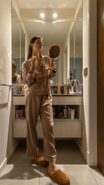 Full length portrait of young woman standing doing makeup