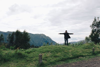 Man with arms outstretched standing on mt bromo against cloudy sky