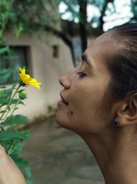 Profile view of woman smelling yellow flower blooming on plant