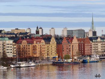 Sailboats in river by buildings in city against sky