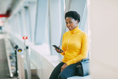 Attractive african girl is waiting for a train in the subway and listening to music with headphones.