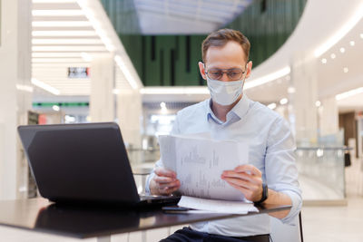 Businessman wearing mask working while sitting at mall