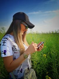 Young woman using mobile phone on field against sky