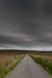 Road passing through landscape against storm clouds