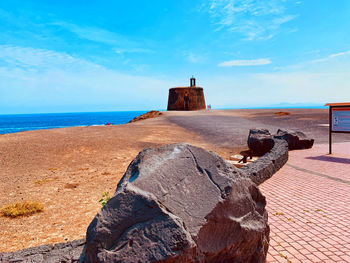 Shadow of rocks on beach against blue sky