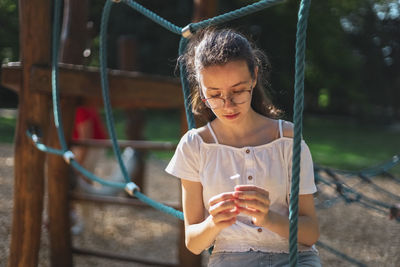 A caucasian teenage girl sits on a rope swing and looks thoughtfully and at a daisy in her hands